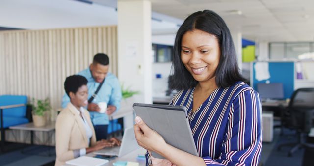 This stock photo features an African American businesswoman actively using a tablet at a modern office. Ideal for business-related designs, presentations, corporate brochures, and advertisements focusing on professional environments, technology in business, diversity in the workplace, and women in leadership roles. The image can also enhance blog posts about modern office practices, digital tools for business, and effective workplace collaboration.