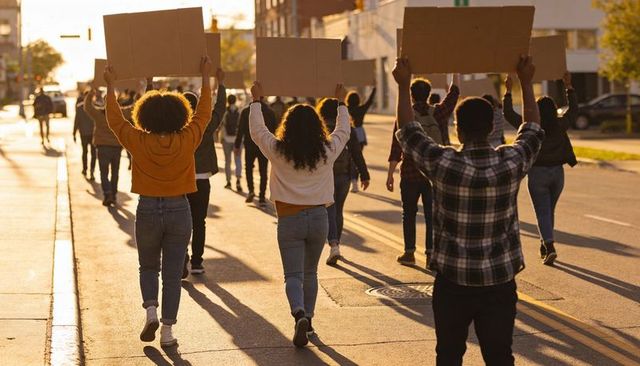 Marching protesters holding blank cardboard signs at golden hour on urban street
