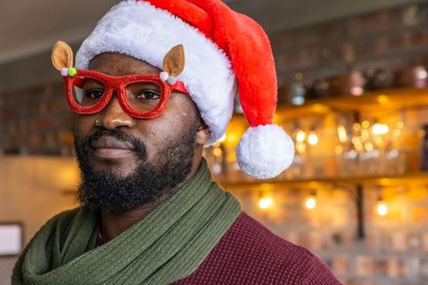African american man celebrating wearing santa hat and reindeer glasses at cozy bar
