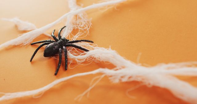 Close up of spider toy forming a spider web against orange background. halloween festivity and celebration concept