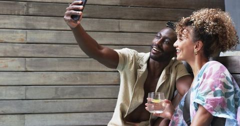 Couple taking selfie on wooden bench smiling and enjoying lemon drink on outdoor patio