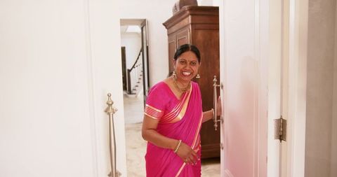 Smiling indian woman in traditional pink sari welcoming guests at home