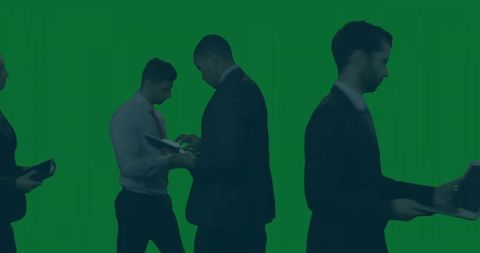 Business team silhouettes collaborating with laptops and tablets on green chroma backdrop