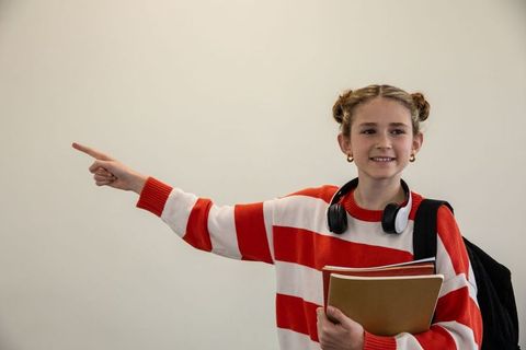 Smiling student pointing with books and headphones