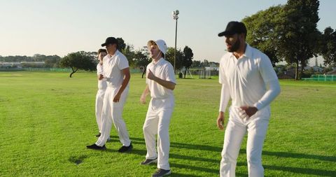 Diverse Cricket Team Warming Up on Sunlit Grass Field Wearing White Uniforms and Caps