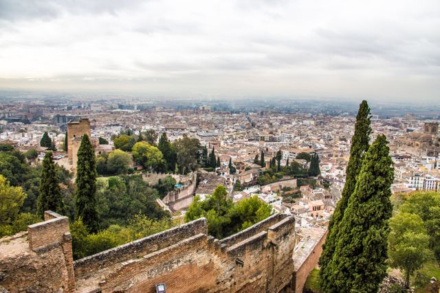Capturing a sweeping panoramic view of Granada, this image showcases the city's intricate blend of historical landmarks such as the famous Alhambra, nestled within rolling hills and lush greenery. The dense urban fabric is contrasted by the surrounding mountainous landscape, making this perfect for travel and tourism promotions, cultural heritage projects, and educational material on Spanish history and geography.
