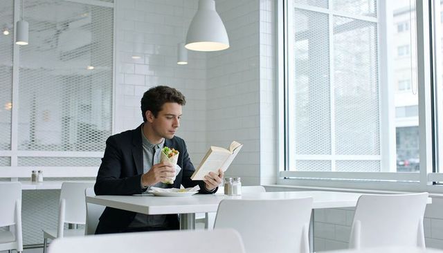 Young professional reading while enjoying fresh wrap in bright minimalist urban cafe