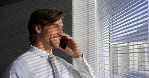 Confident Businessman Discussing on Phone at Bright Office Window