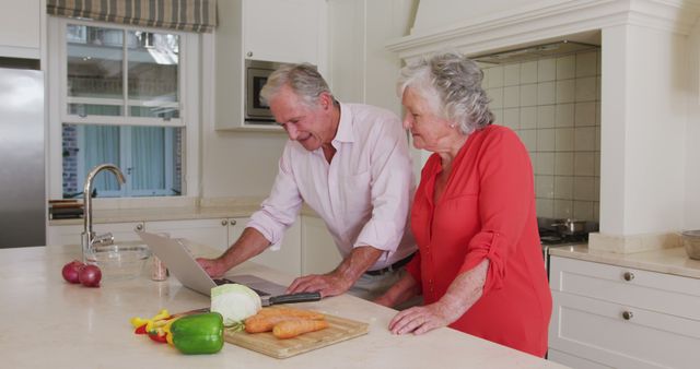 Happy caucasian senior couple in kitchen using laptop for recipe before preparing meal. at home in isolation during quarantine lockdown.