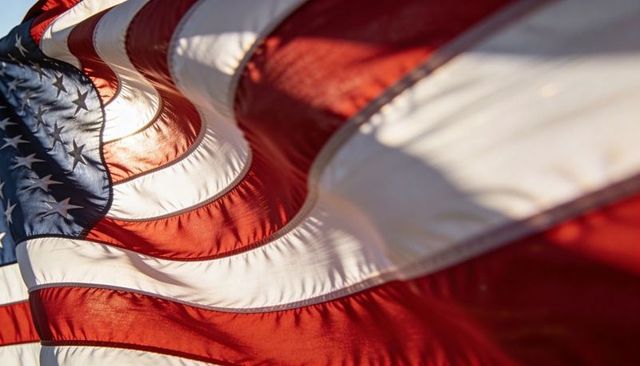 Sunlit rippling american flag closeup showing stars, stripes, texture and stitched seams waving