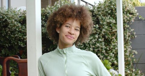 African american woman smiling on covered porch wearing light green zip-up top and natural afro