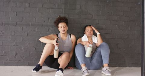 Post-workout friends resting on gym floor holding water bottles and towel