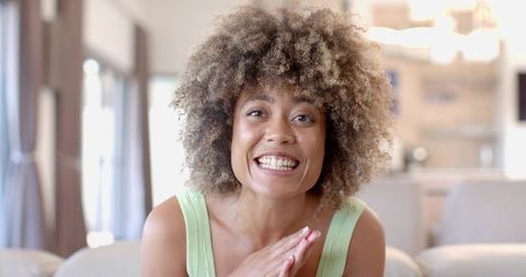 African american woman smiling and clasping hands on sofa in bright living room