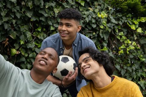 Multiethnic teen friends smiling, posing, holding soccer ball and smartphone outdoors