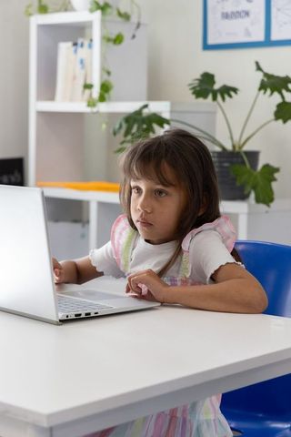 Young girl concentrating on laptop while studying at minimalist home desk with plants