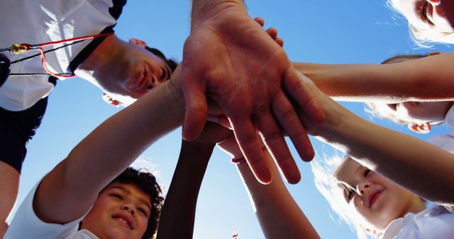 A diverse group of children and an adult stack their hands together in a gesture of teamwork and unity, with copy space. This symbolizes collaboration and support, often seen in sports or group activities to motivate and bond participants.