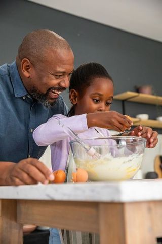 African american father teaching daughter baking together in bright modern kitchen
