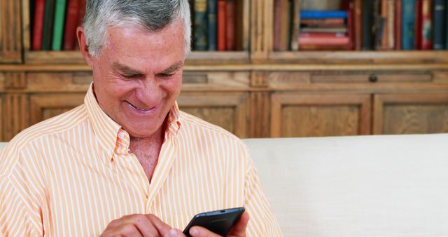 Smiling Senior Man Using Smartphone and Sitting on Couch, Wood Bookshelves - Download Free Stock Images Pikwizard.com