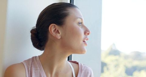 Serene african american woman gazing out sunlit window with bun and casual top