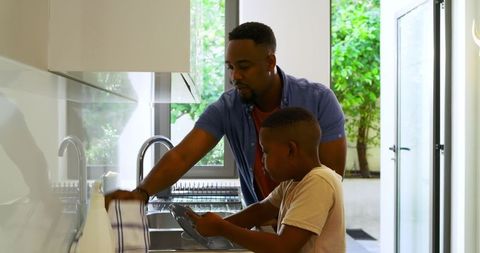 Father and Son Cleaning Dishes in Modern Kitchen