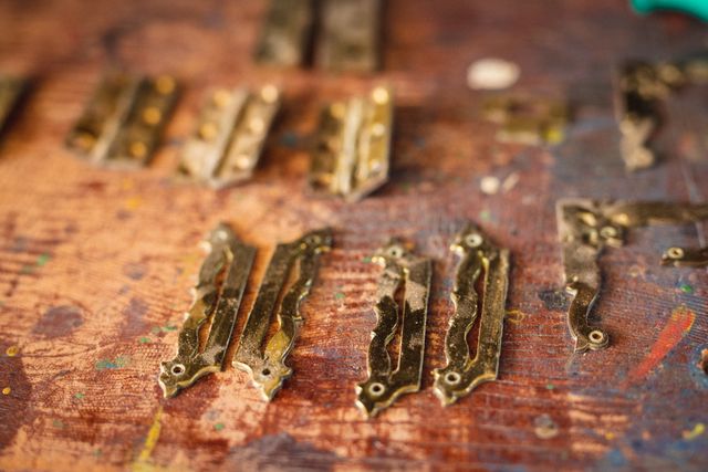 Detailed close-up of decorative metal hinges on a workshop table, ideal for illustrating concepts related to carpentry, woodworking, and metalworking. Useful for blogs, articles, or advertisements focusing on craftsmanship, DIY projects, and artisan hardware.