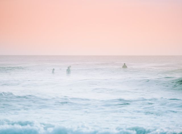 People enjoying a calm ocean at sunrise. Soft pastel colors create a serene and peaceful atmosphere. Perfect for use in travel brochures, relaxation promotes, wellness blogs or background imagery in presentations on nature and tranquility.