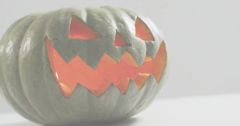 Glowing carved pumpkin casting warm orange light on white tabletop