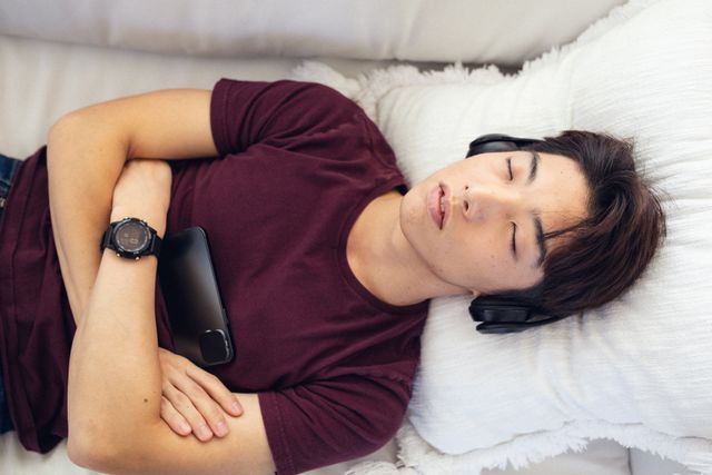 Directly above shot of asian teenage boy napping while listening music on couch at home - Download Free Stock Photos Pikwizard.com