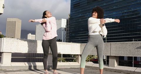 Diverse female friends stretching on rooftop, warming up for urban workout with smartwatch
