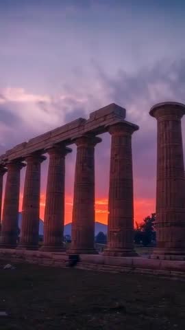 Vertical video showing sun aligning between ancient colonnade at dusk, casting starburst flare