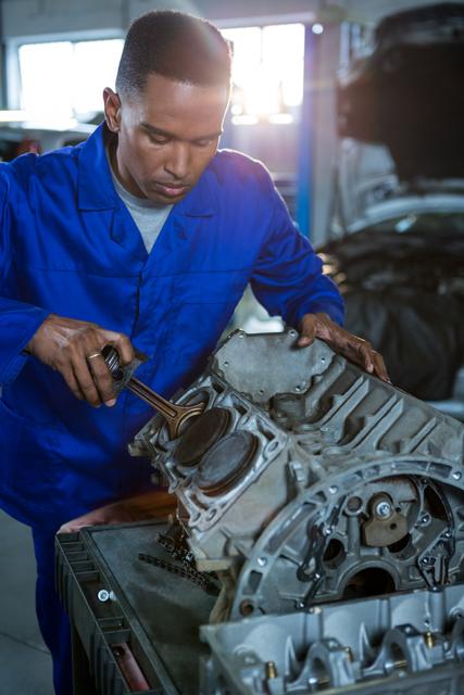 Mechanic in blue overalls repairing a car engine in a garage. Ideal for use in automotive repair advertisements, mechanical engineering articles, and professional training materials.