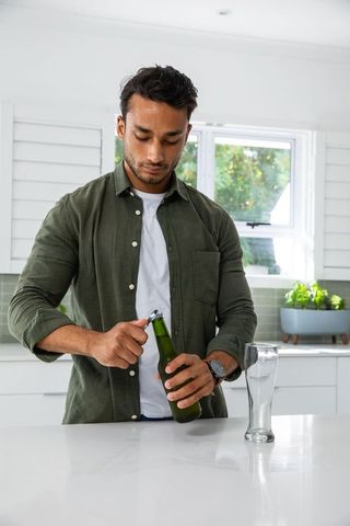 Man opening green glass bottle in modern kitchen