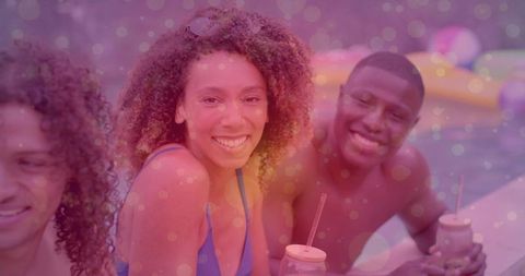 Smiling woman sitting poolside holding mason jar drink with friends enjoying summer float party
