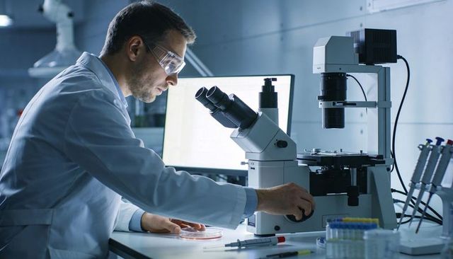 Researcher adjusting microscope for cellular analysis in modern biotechnology laboratory