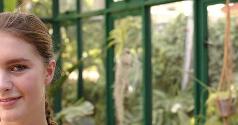 Woman Smiling in Lush Greenhouse Surrounded by Greenery