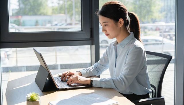 Young professional typing on tablet laptop in sunlit minimalist office with succulent