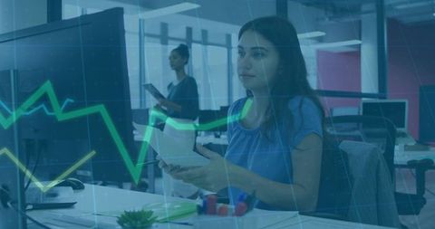 Young professional reviewing data with tablet and monitor, analytics overlay in office