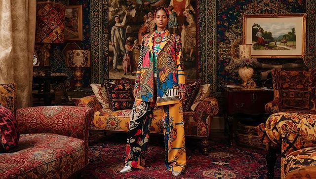 Wearing bold printed suit in opulent Victorian salon with tapestries and velvet decor