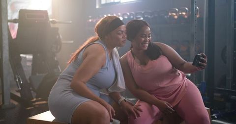 Diverse women taking gym selfie after workout wearing pink and blue activewear