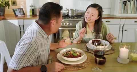 Asian couple enjoying cozy candlelit dinner at home sharing stew and red wine
