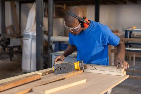 African american carpenter using electric planer in woodworking workshop