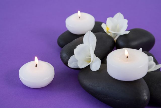 White flowers, candles on zen stone on purple background