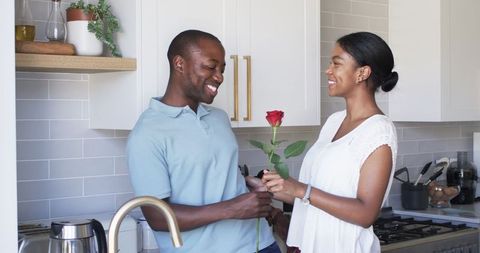 Smiling Couple Sharing Affectionate Moment Holding Red Rose in Kitchen
