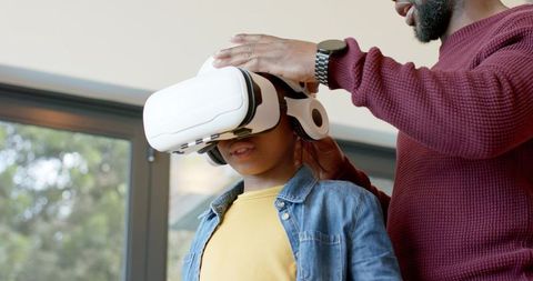 African american father adjusting vr headset for son exploring virtual reality at home