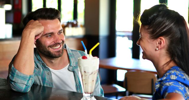 Happy couple interacting while having milkshake in pub