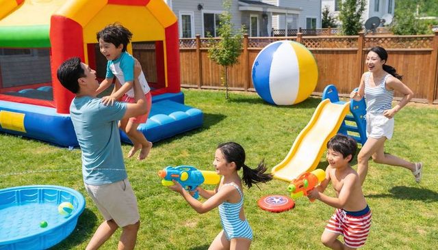 Family enjoying backyard summer party, kids playing water guns and inflatable bounce house