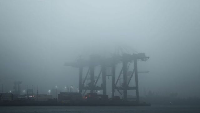 Towering container cranes rising through heavy fog at industrial port quay