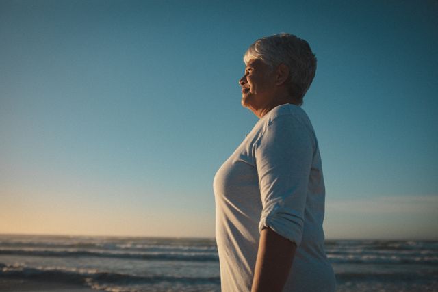 Happy african american senior female looking toward sea during sunset. summer beach vacation by the sea.