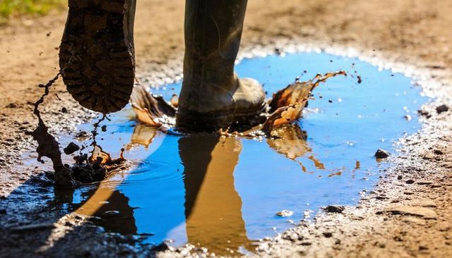 Rubber wellies kicking muddy puddle splashing water and sky reflection on dirt track