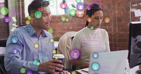 Colleagues collaborating at laptop with colorful chat bubbles overlay in modern brick office